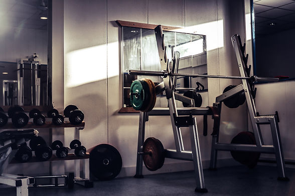 A squat rack and dumbbells in a gym with a low lit filter